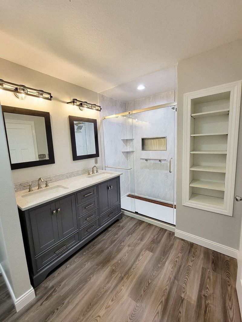 Remodeled bathroom with a dark vanity, wood-look floor and new walk-in shower