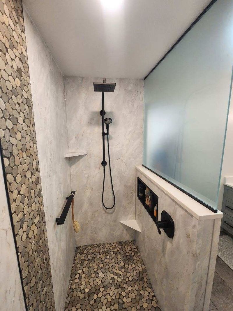 Walk-in shower with pebble floor, marble-look walls, grab bar and glass half wall