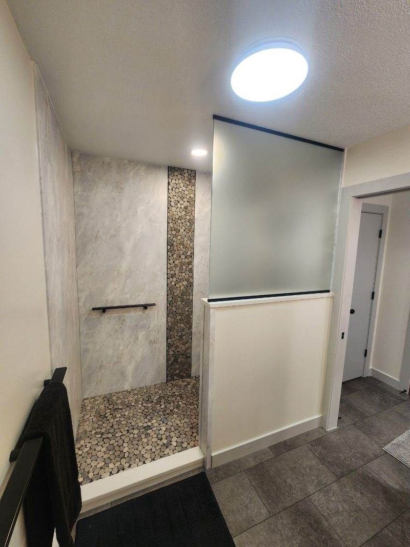 Walk-in shower with pebble floor and frosted glass half wall
