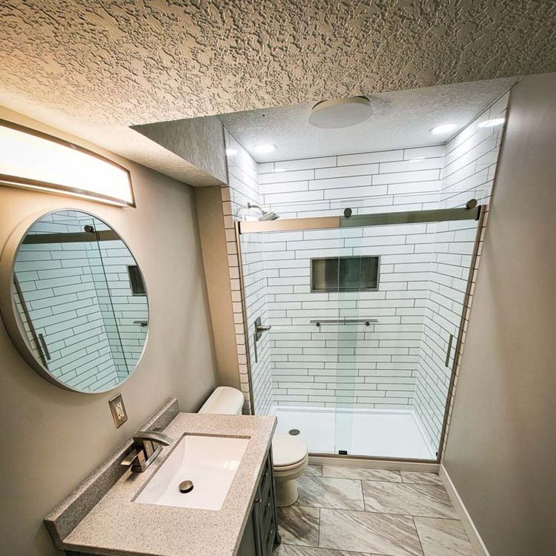 Full bathroom remodel with a white tile-look acrylic shower and round mirror
