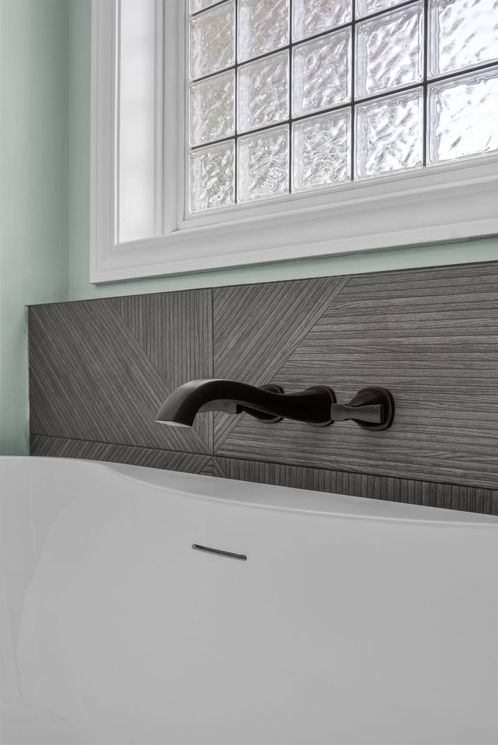 Freestanding tub with gray tile-look accent wall beneath a glass block window